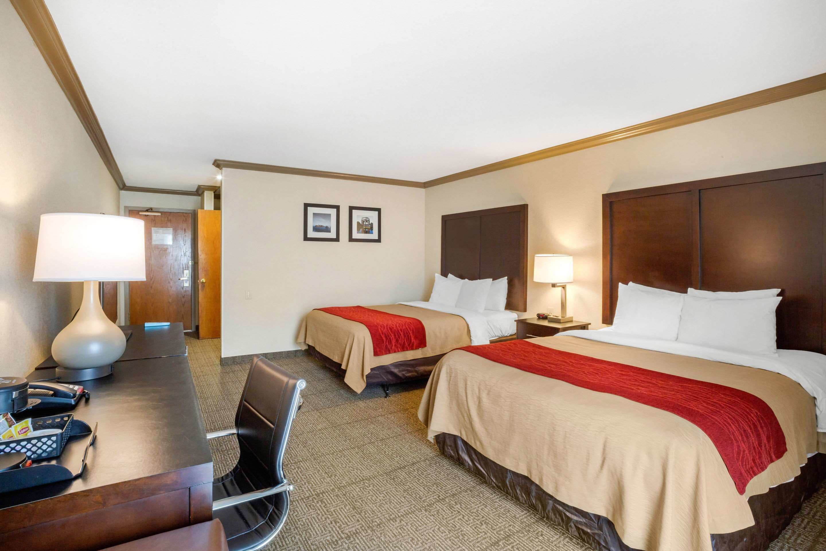 A hotel room with two beds, a desk with a lamp, a chair, and a telephone.