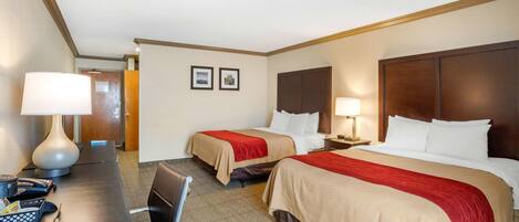 A hotel room with two beds, a desk with a lamp, a chair, and a telephone.