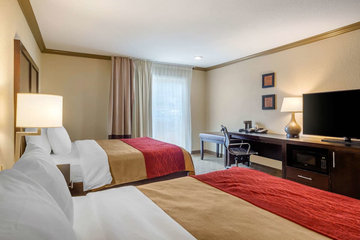 A hotel room with two beds, a desk, a television, and a microwave.