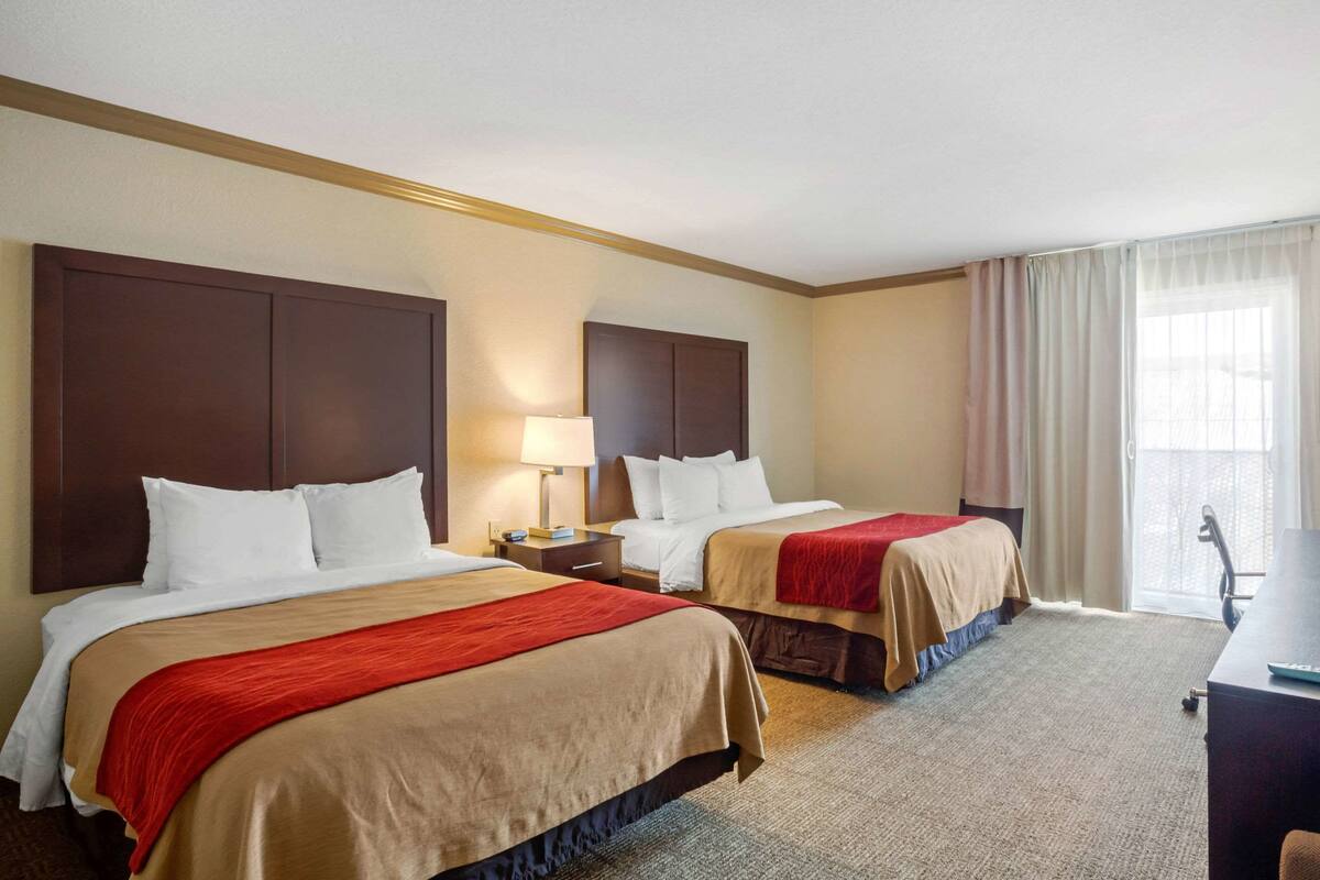 A hotel room with two beds, a desk, and a window with curtains.