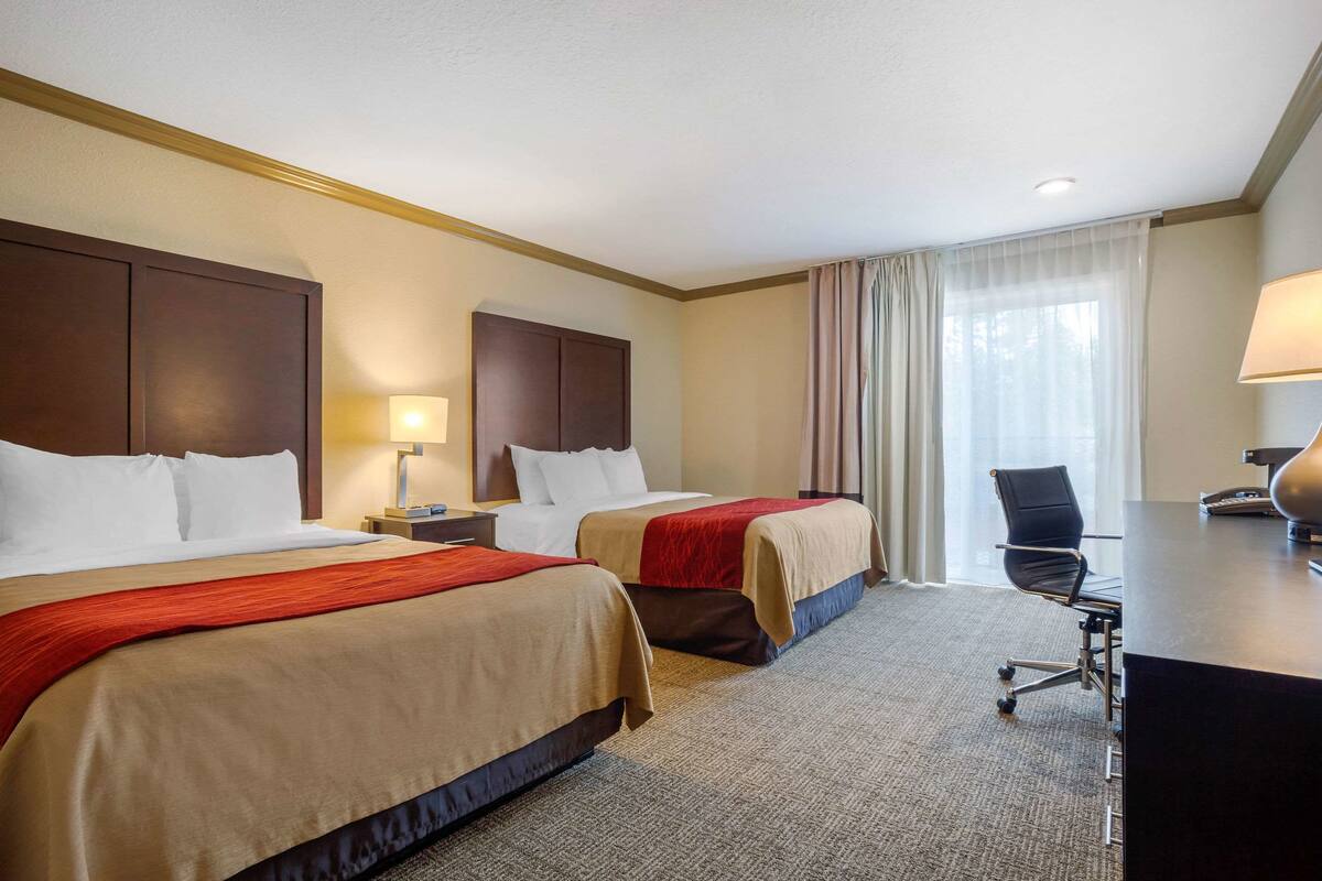 A hotel room with two beds, a desk, a chair, and a window with curtains.