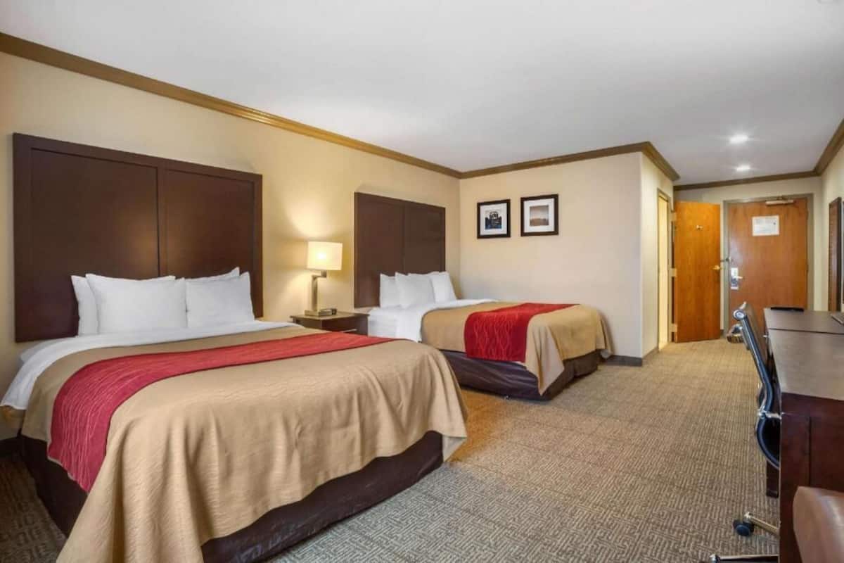 A hotel room with two beds, a desk, and a door.