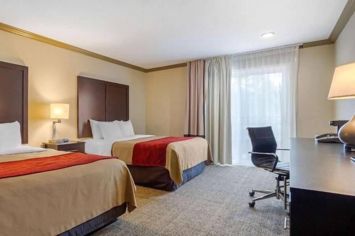 A hotel room with two beds, a desk, a chair, and a window with curtains.