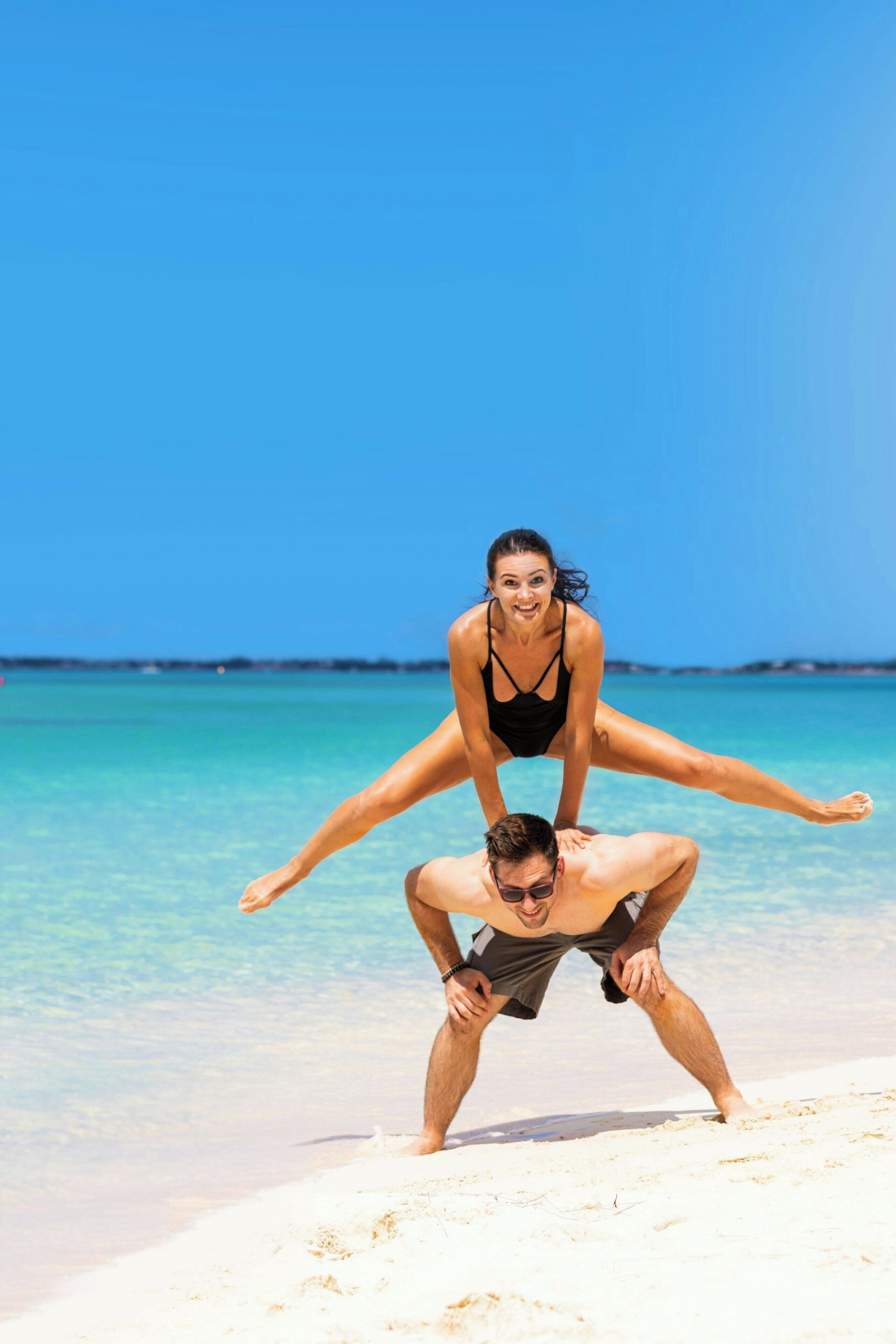 A man and a woman on a beach with clear blue water and a clear sky.