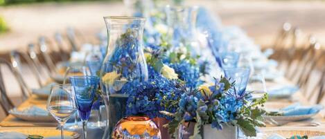 A table set for a meal with blue and white tableware, clear glassware, and floral centerpieces.