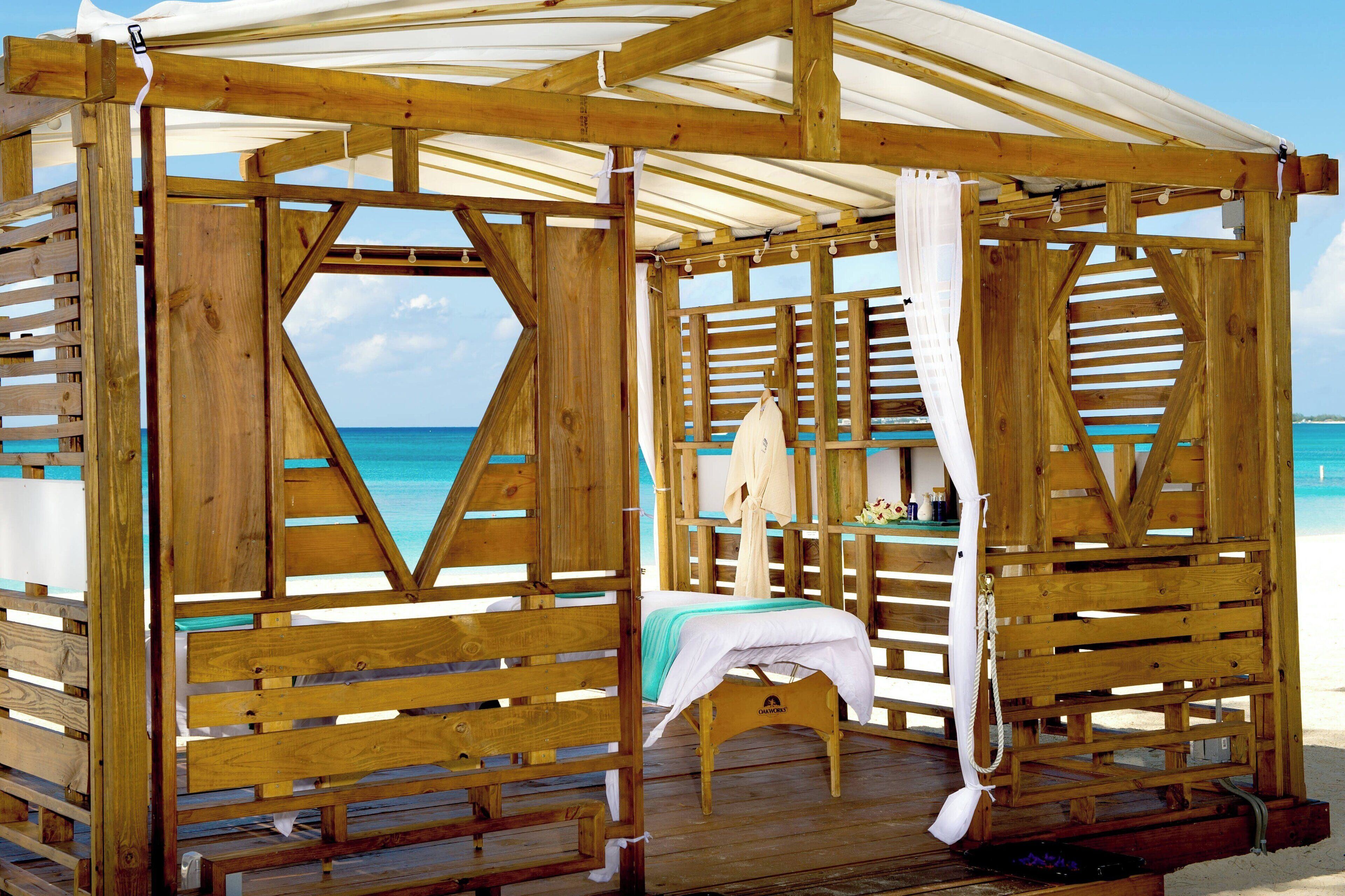Een houten strandhut met een bed, een tafeltje en een bank.