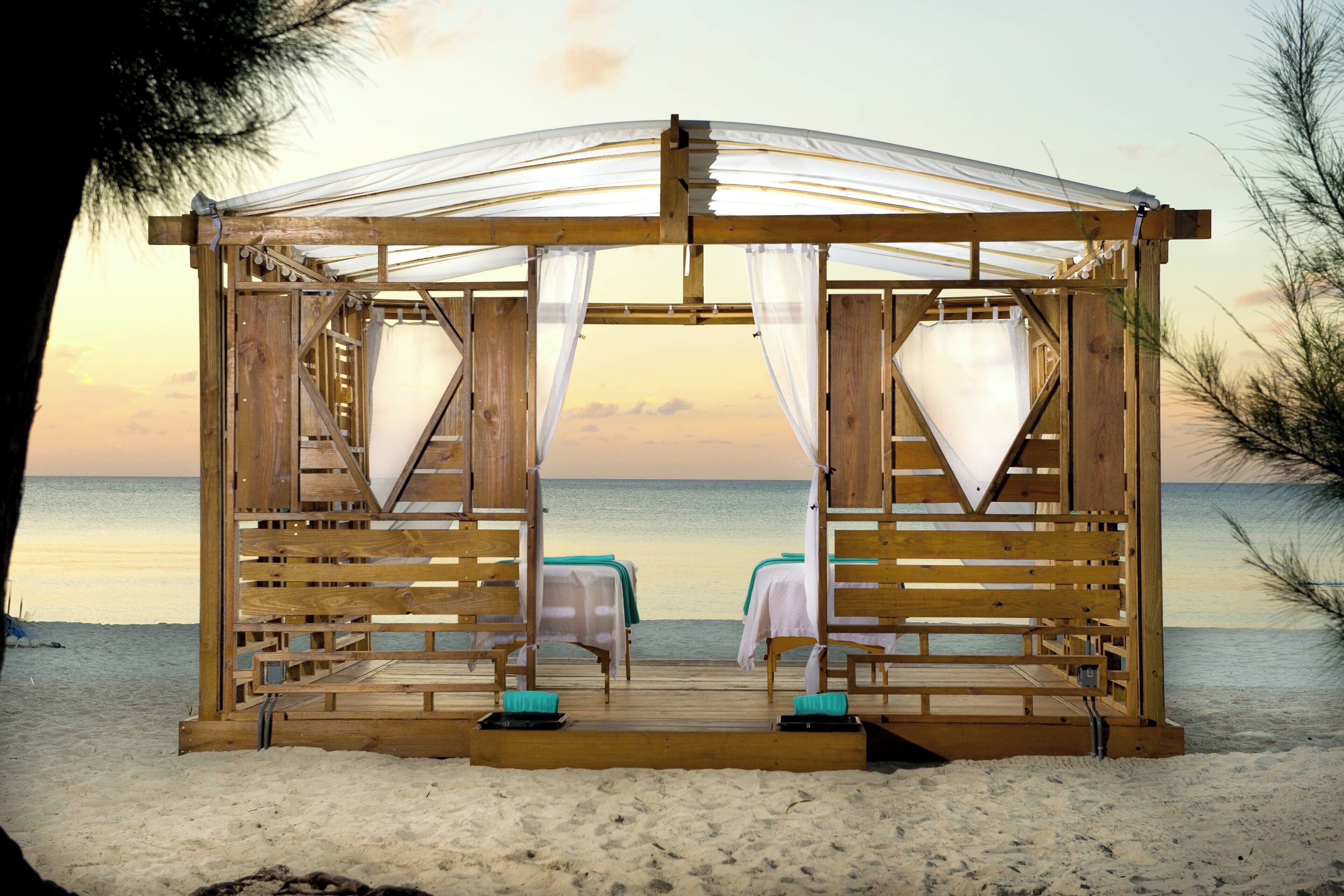 A wooden beach cabana with two beds, a canopy, and a view of the sea.