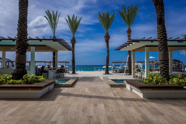 A beachside resort with a wooden deck, palm trees, and a view of the ocean.