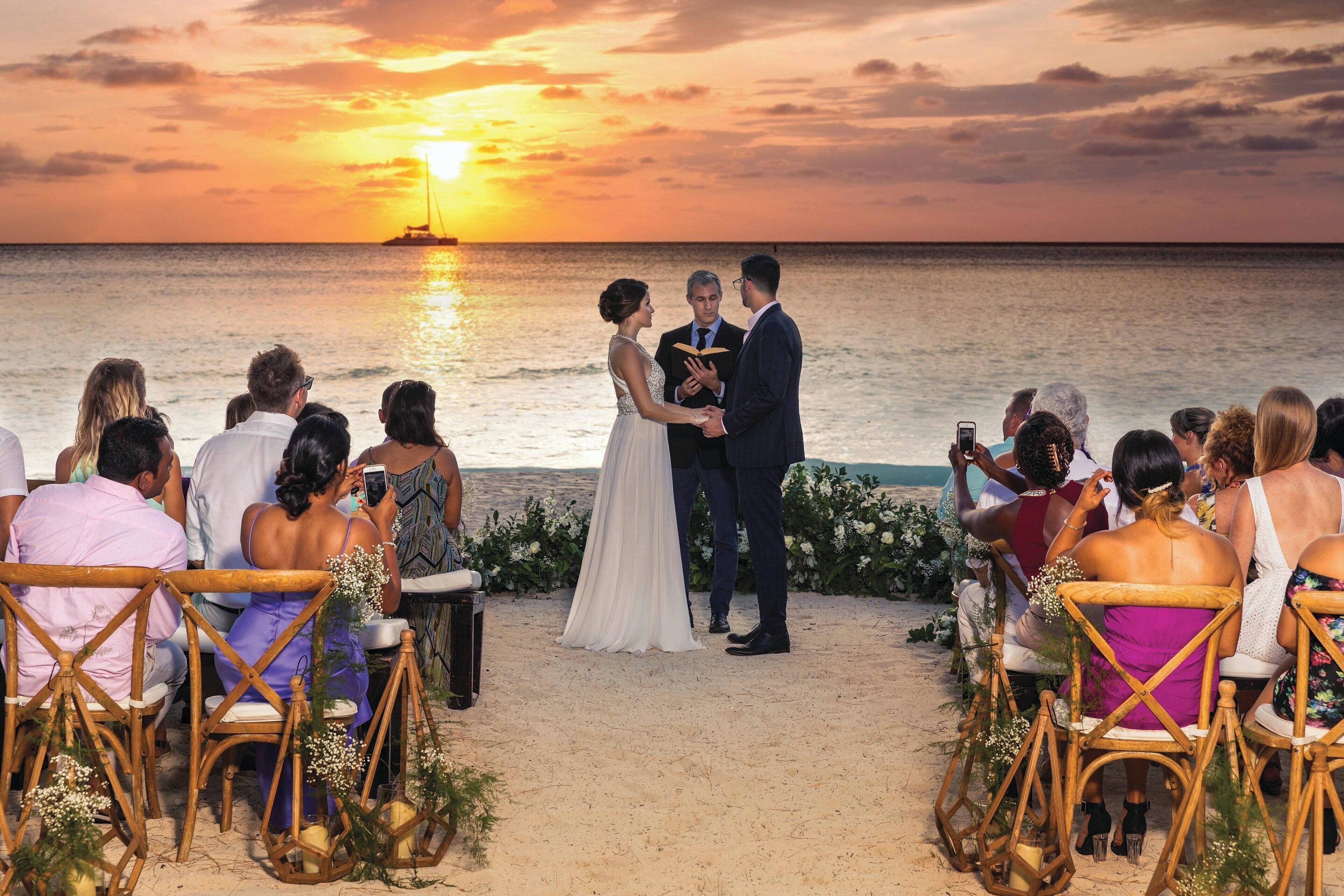 A wedding ceremony on a beach with a sunset view.