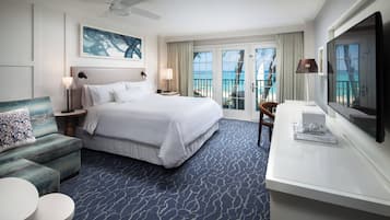 A hotel room with a large bed, a sofa, a TV, and a balcony with a view of the ocean.