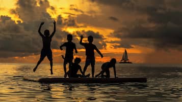 A silhouette of people on a surfboard against a sunset.