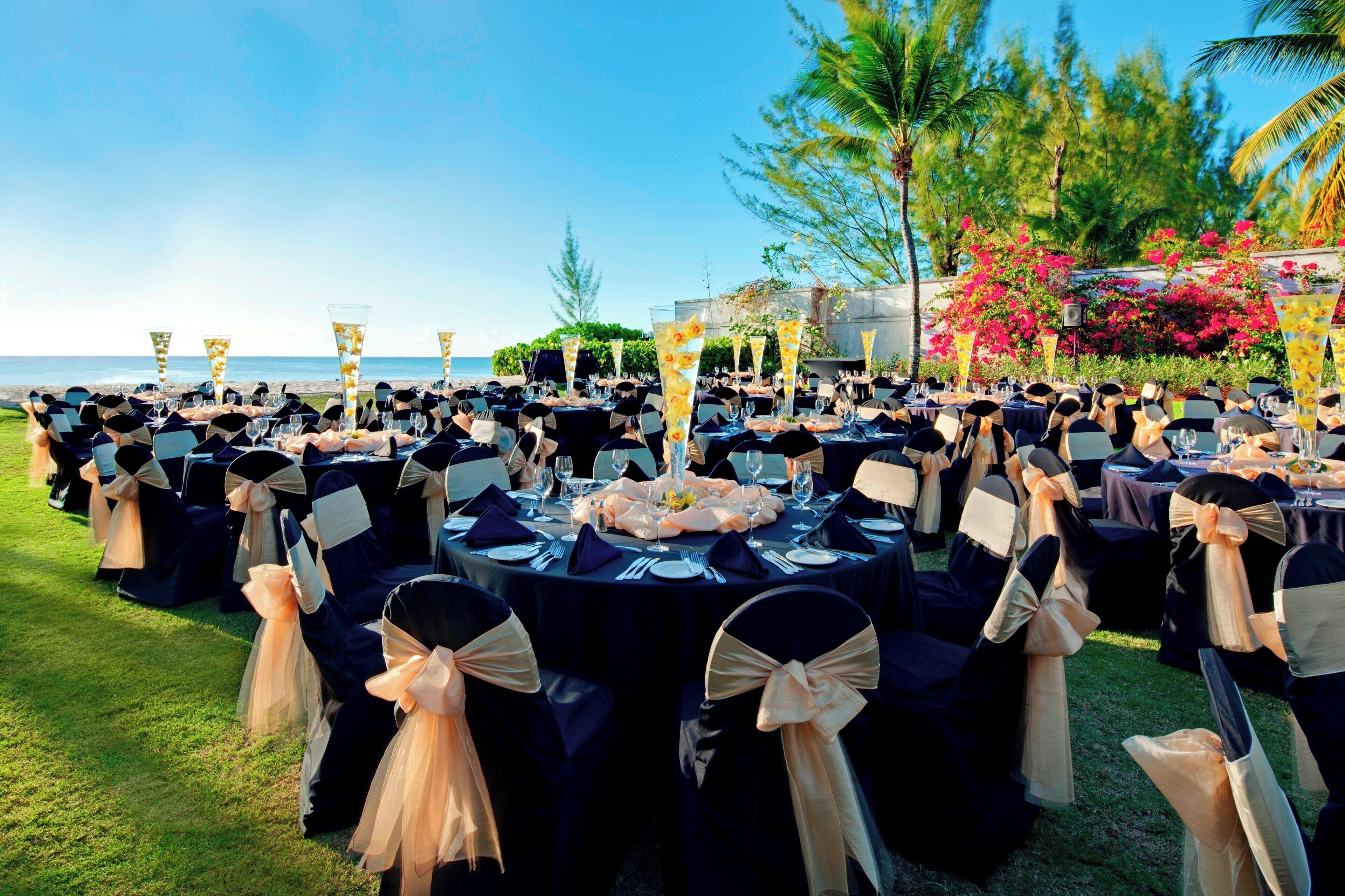 An outdoor dining area with round tables, black tablecloths, and chairs with beige sashes.