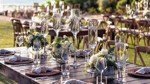 A wooden table set for a formal outdoor event with clear glassware, white napkins, and floral centerpieces. - The Westin Grand Cayman Seven Mile Beach Resort & Spa (Seven Mile Beach)