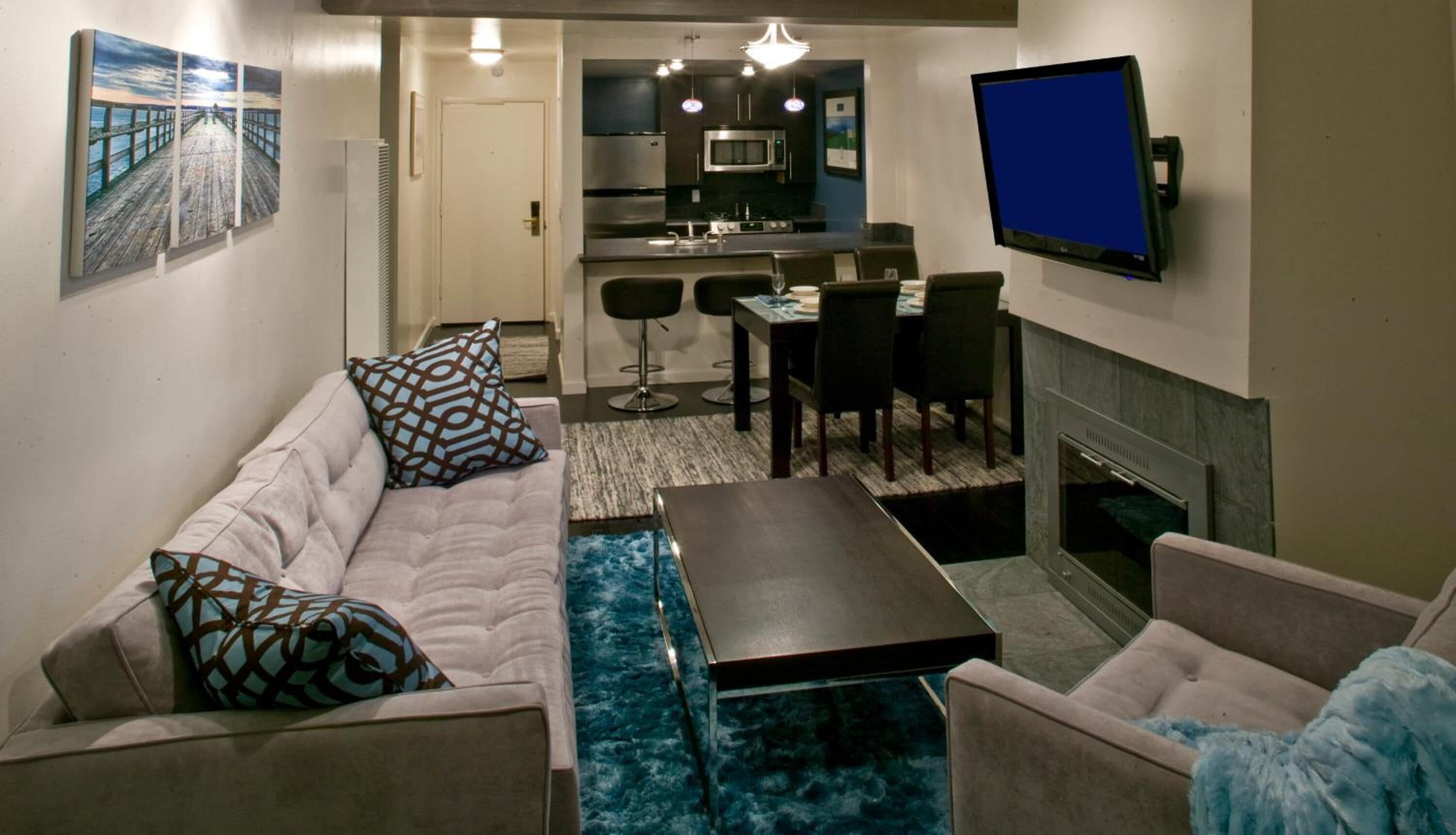 Una sala de estar con sofá, sillones, una mesa de centro, televisor, chimenea y una zona de cocina con microondas y taburetes de bar.