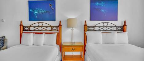 A hotel room with two beds, a nightstand with a lamp, and two wall-mounted artworks.