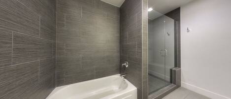 A modern bathroom with a freestanding bathtub, a glass-enclosed shower, and dark tiled walls.