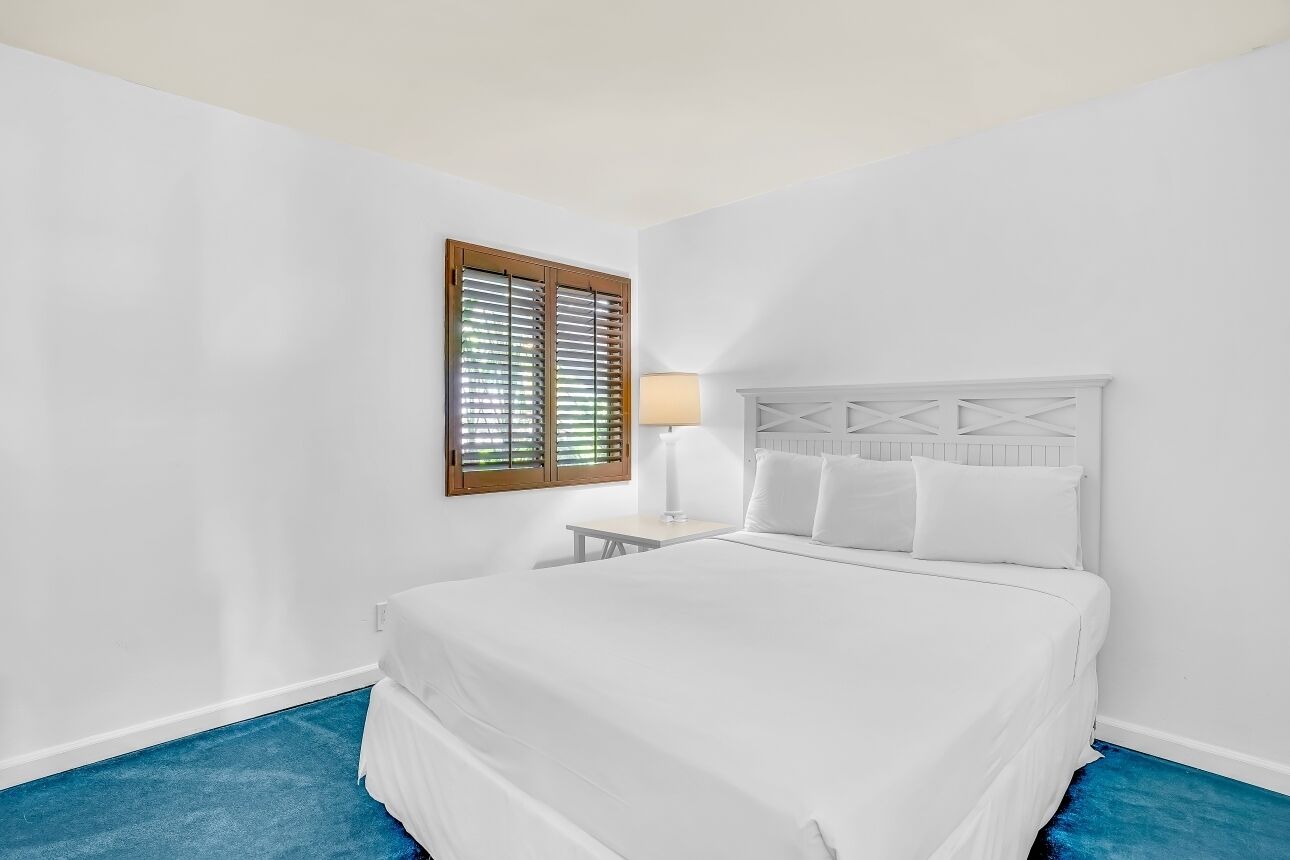 A bedroom with a bed, a nightstand, a lamp, and a window with blinds.