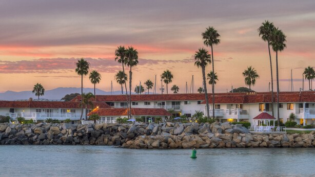 A beachfront hotel with multiple buildings, palm trees, and a rocky shoreline. - Oceanside Marina Suites (Oceanside)