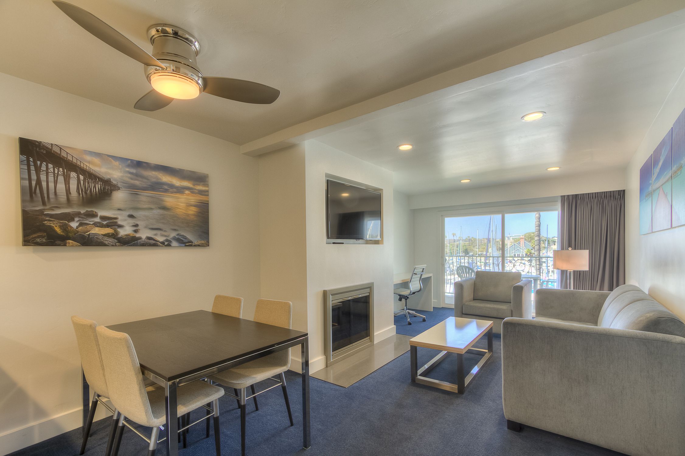 A hotel room with a dining table, chairs, a sofa, a fireplace, a TV, and a balcony with a view.