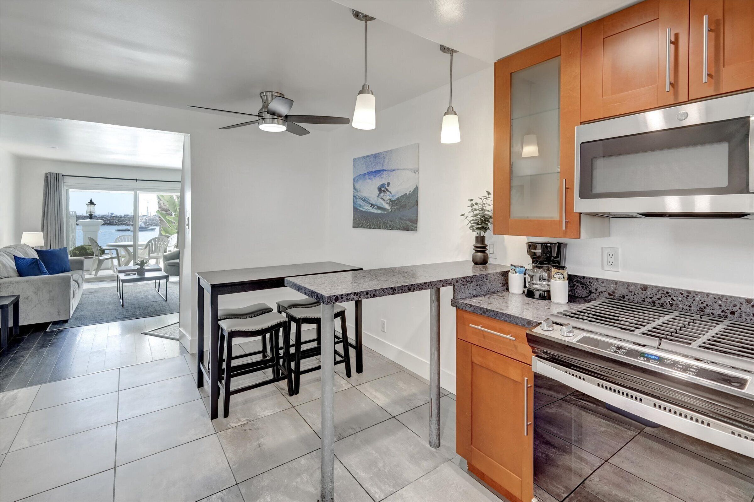 Una cocina moderna con una isla central, microondas y estufa. Hay una zona de comedor con una mesa y sillas, y vistas al mar a través de amplios ventanales.