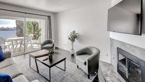 A modern living room with a fireplace, a flat-screen TV, and a view of the sea. - Oceanside Marina Suites (Oceanside)