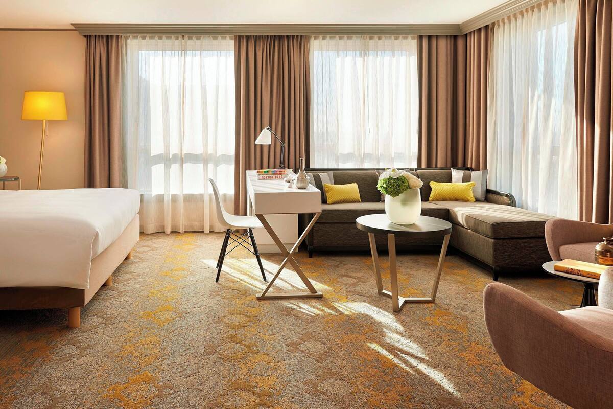 Quarto de hotel com cama, escrivaninha, sofá e poltrona.