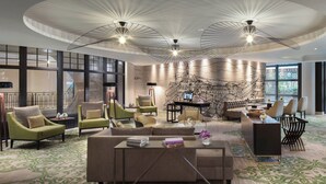 A modern hotel lobby with a curved ceiling, green and beige seating, a central coffee table, and a mural of Paris. - Renaissance Paris La Defense Hotel (Puteaux)