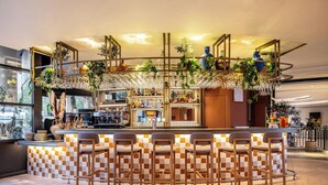 A bar area with a checkered tile backsplash, multiple bar stools, and a variety of plants and decorative items. - Renaissance Paris La Defense Hotel (Puteaux)