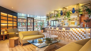 A modern living room with a glass coffee table, sofas, and a kitchen area with bar stools and a checkered backsplash. - Renaissance Paris La Defense Hotel (Puteaux)