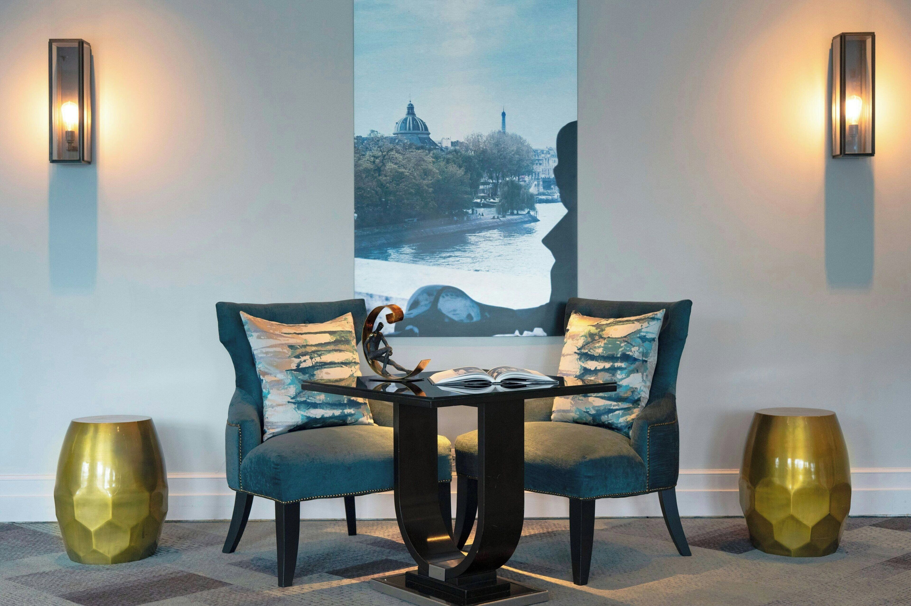 Un área de estar moderna con un sofá y una mesa, dos lámparas de pared y una pintura de gran formato con un paisaje urbano.