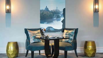 Un área de estar moderna con un sofá y una mesa, dos lámparas de pared y una pintura de gran formato con un paisaje urbano.