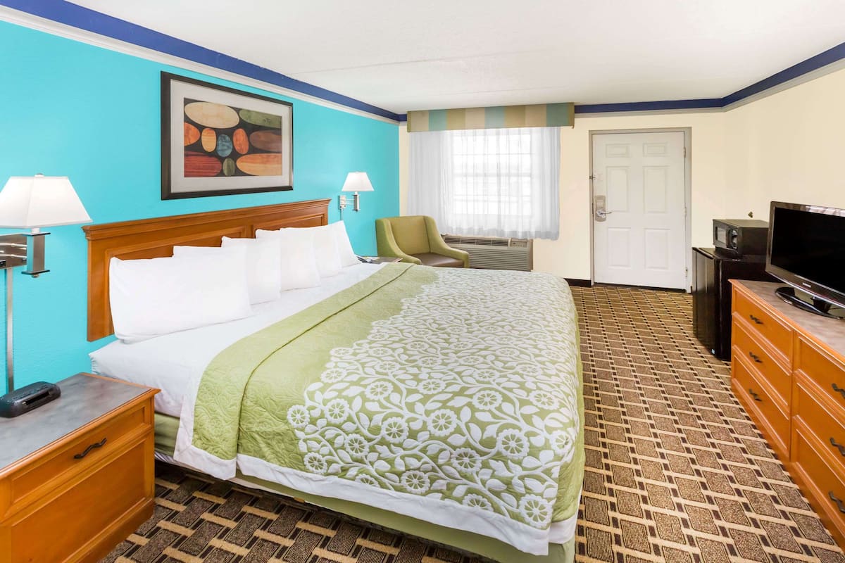 A hotel room with a bed, a chair, a television, and a door.