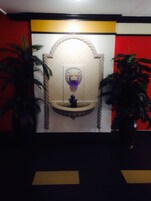 Un baño con pared de azulejos blancos, un lavamanos central con un adorno decorativo y dos plantas en macetas.