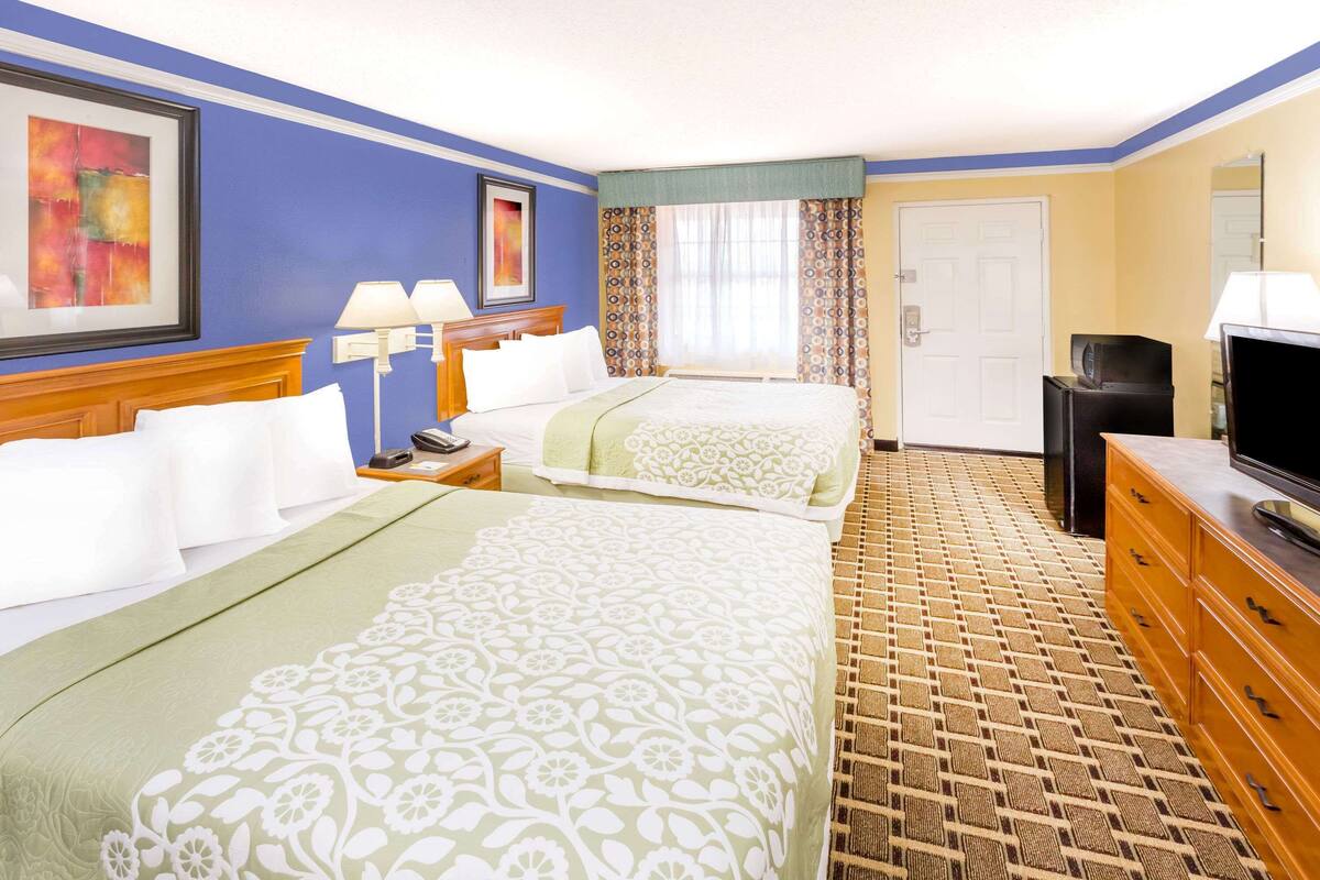 A hotel room with two beds, a television, a desk, and a bathroom.