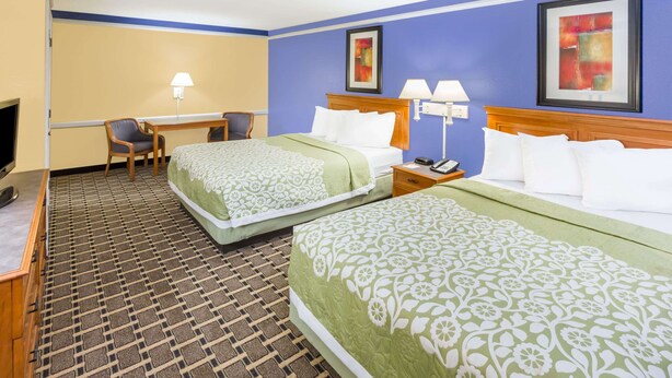 Ein Hotelzimmer mit zwei Betten, einem Schreibtisch, einem Stuhl und einem Fernseher.