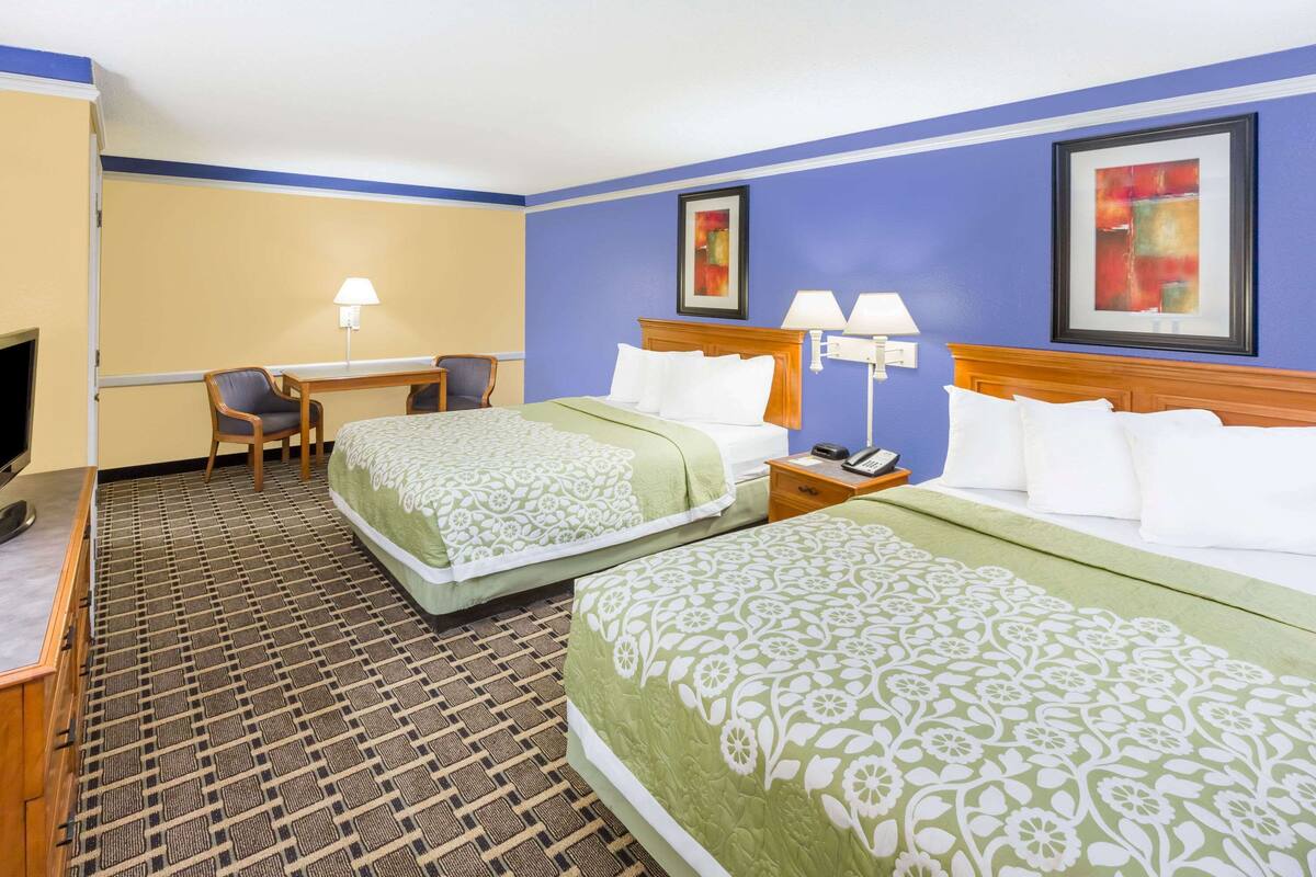 A hotel room with two beds, a desk, a chair, and a television.