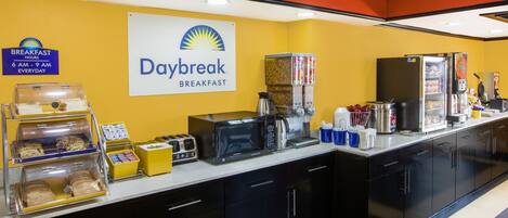 A breakfast area with a sign for Daybreak Breakfast, a coffee machine, a microwave, and various food items.