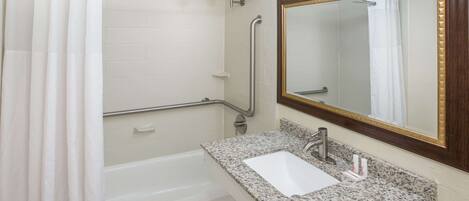 A bathroom with a white bathtub, a granite sink, a mirror with a wooden frame, and a shower with a white curtain.