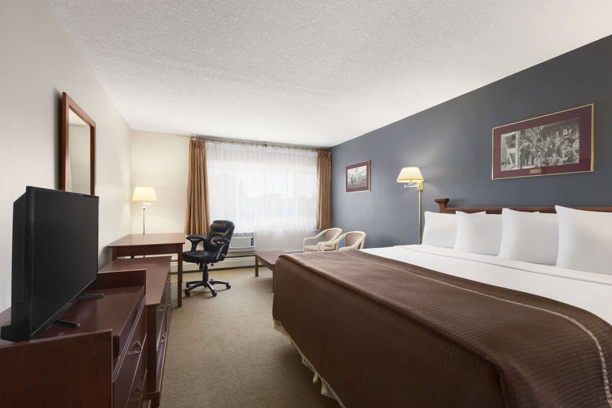 A hotel room with a bed, a desk with a TV, a chair, a lamp, and a window with curtains.