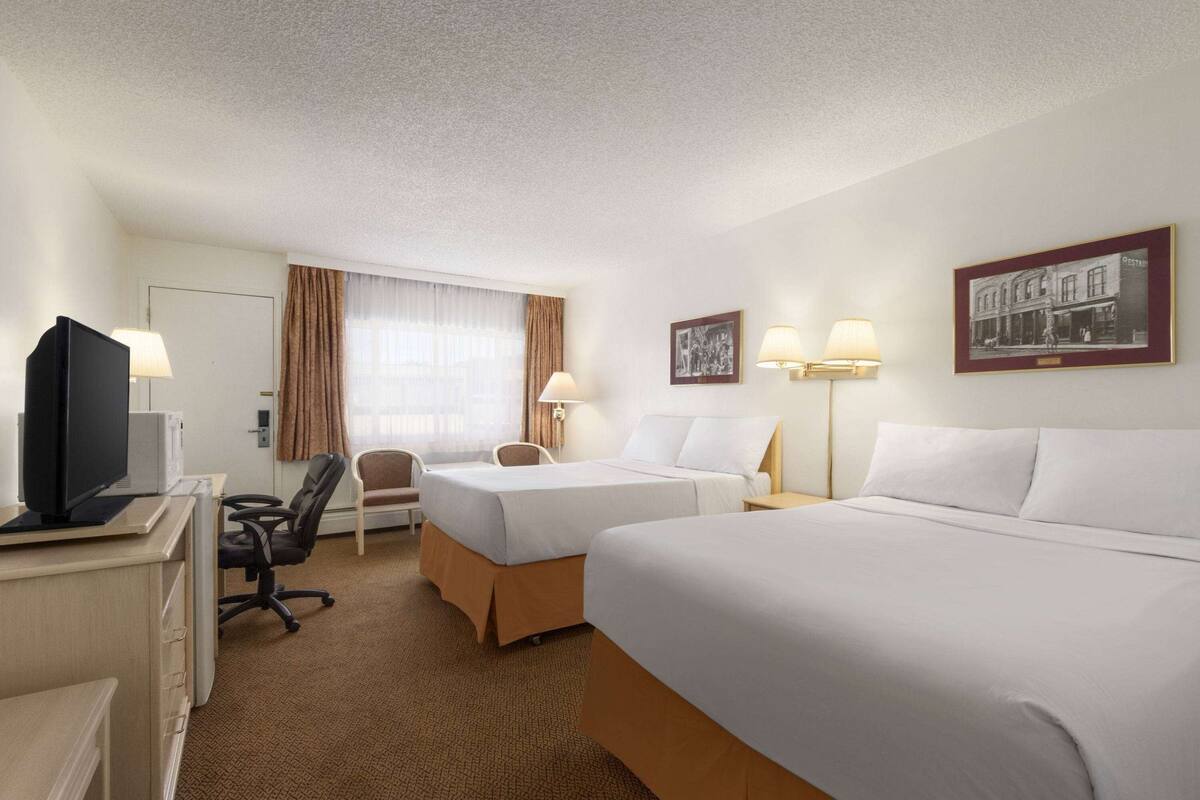 A hotel room with two beds, a desk with a computer, a chair, and two lamps.
