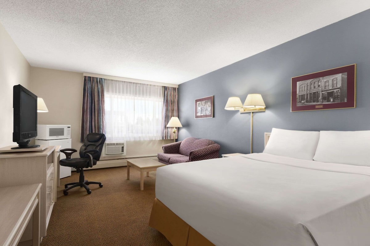 A hotel room with a bed, desk, chair, television, and two lamps.