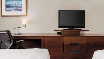 Quarto de hotel com escrivaninha de madeira, televisão, luminária, cadeira e cama.