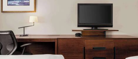 A hotel room with a wooden desk, a television, a lamp, a chair, and a bed.