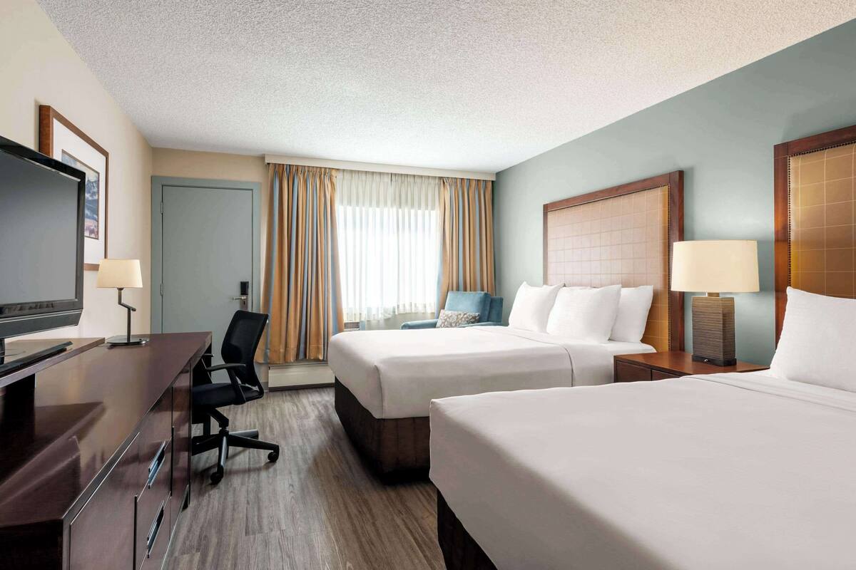 A hotel room with two beds, a desk, a chair, a TV, and a window with curtains.