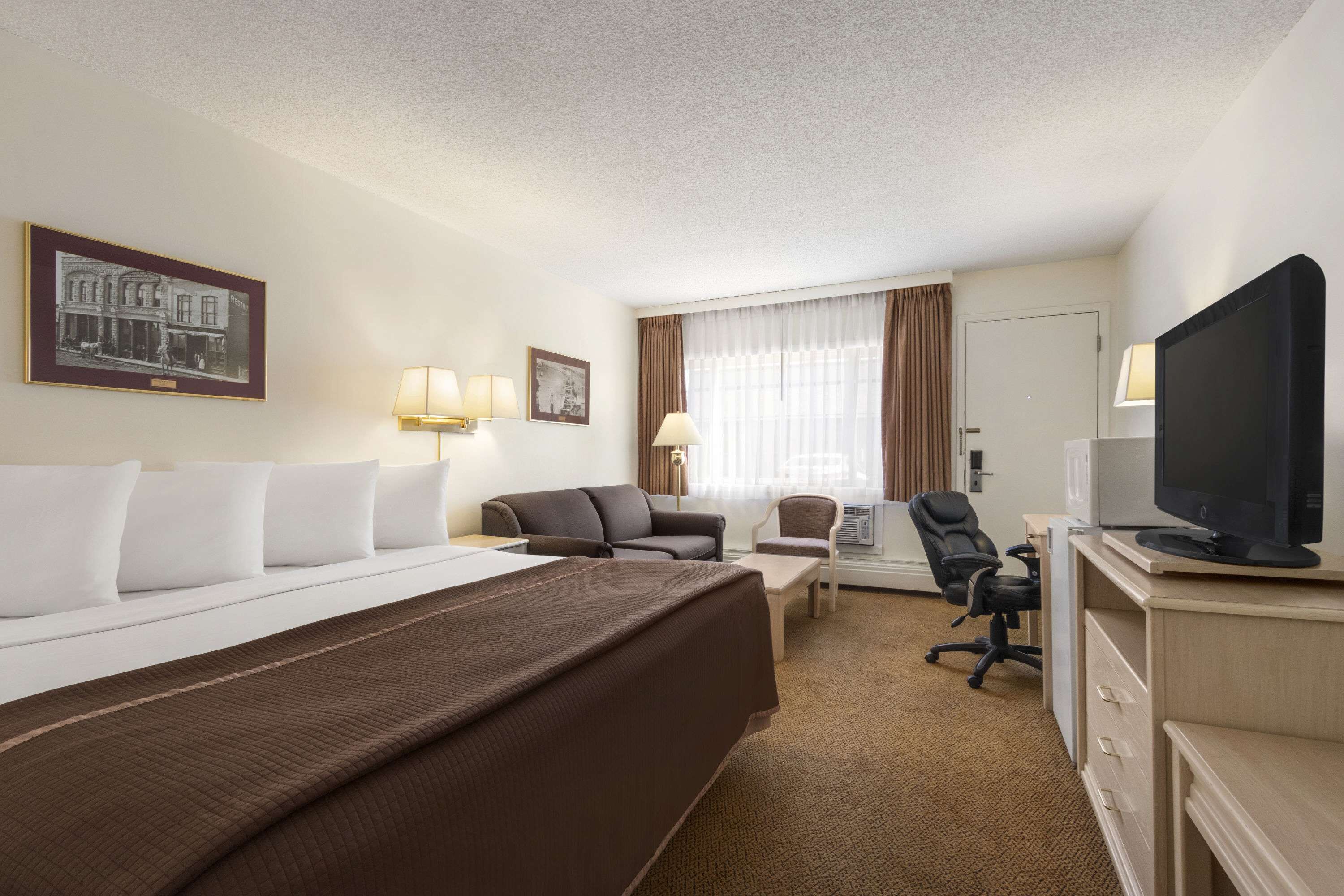 Habitación de hotel con una cama grande, un escritorio con computadora, una silla y un televisor.
