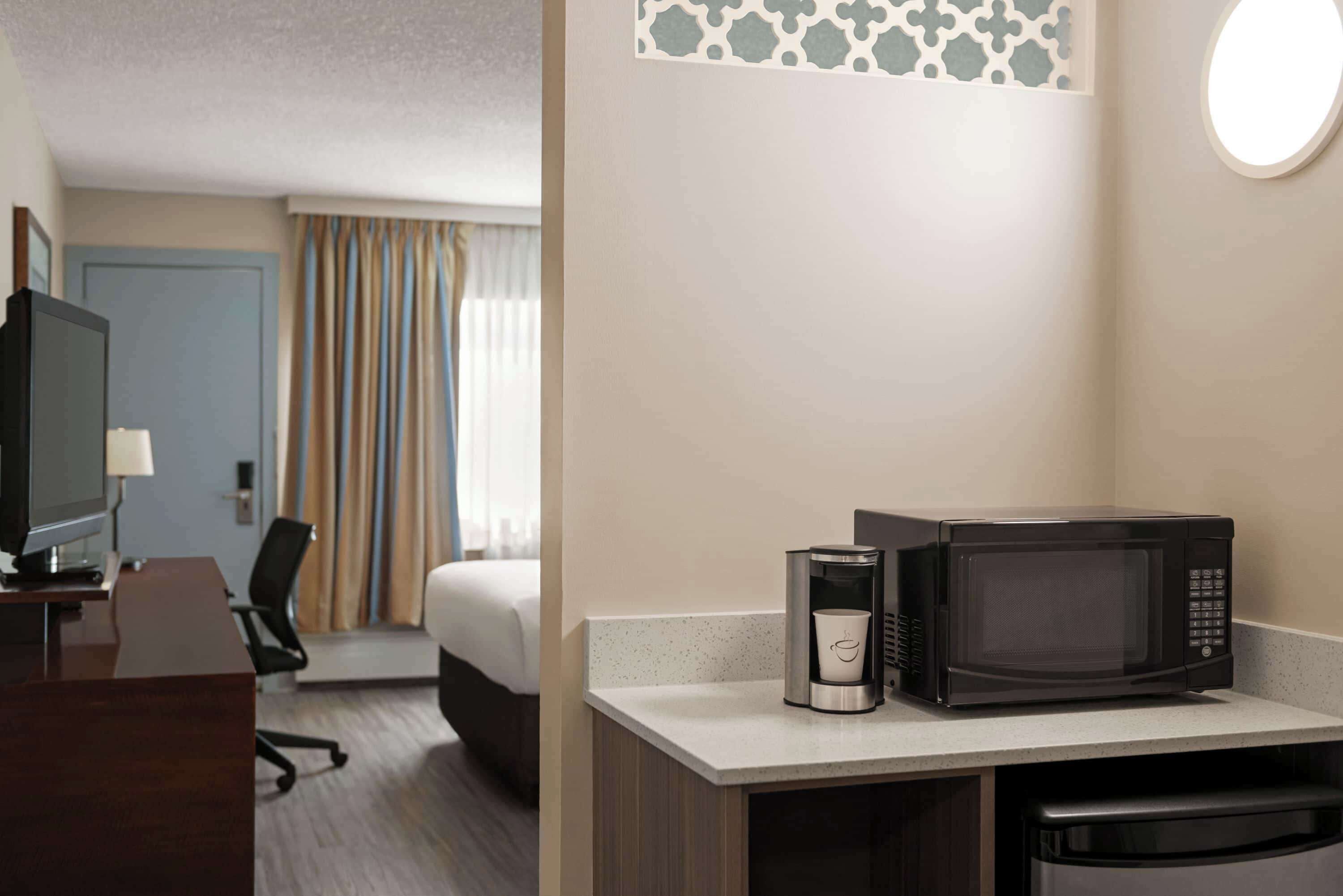 Habitación de hotel con escritorio, televisor, cama, cafetera y microondas.
