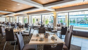 A spacious dining area with multiple tables and chairs, large windows offering views of the outside, and a pool visible through the windows.