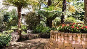 A brick pathway leading through a garden with various plants and a brick wall on one side. - Millennium Hotel Rotorua (Rotorua)