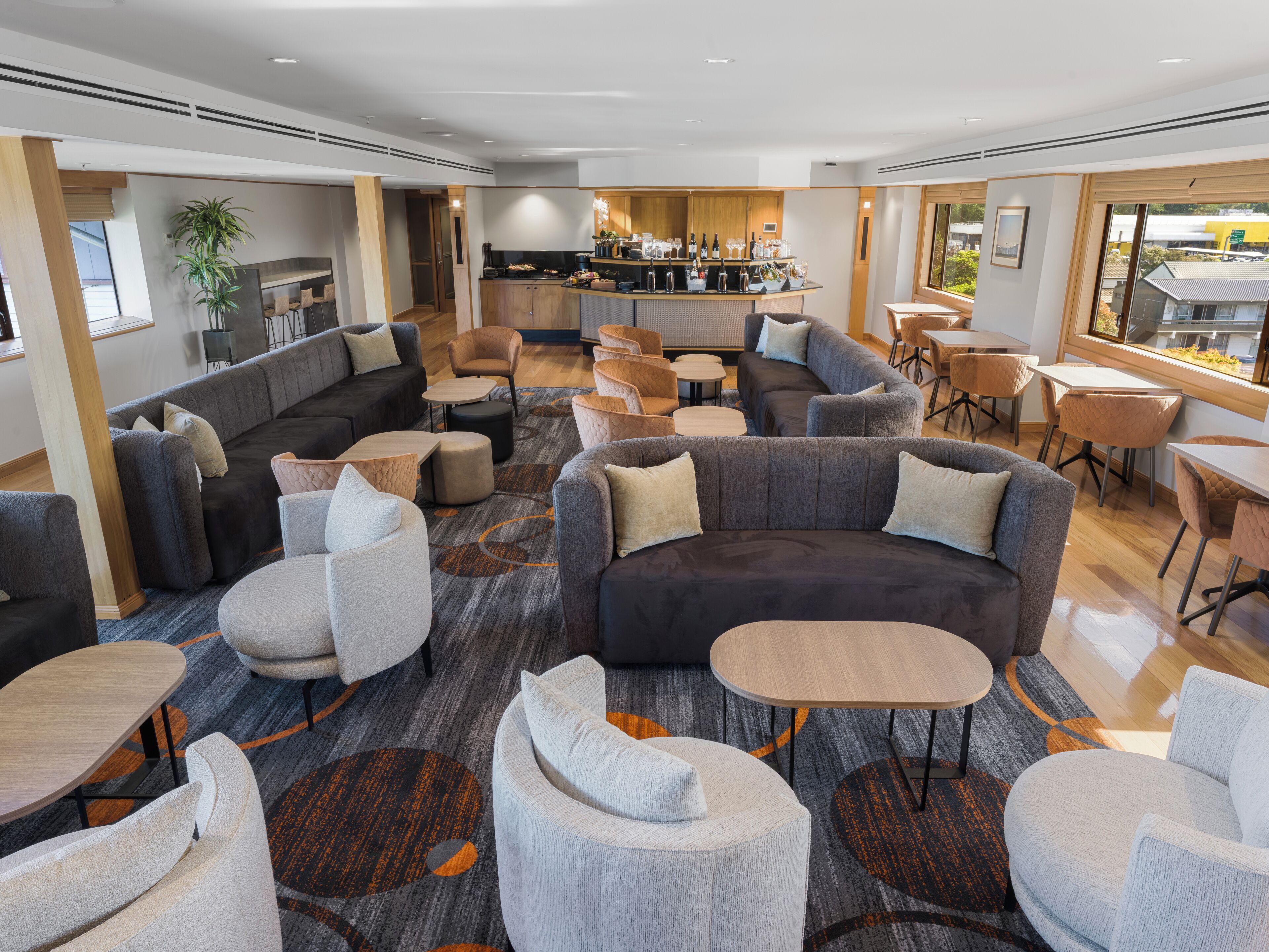 Een moderne hotellobby met een mix van zithoeken, waaronder banken en stoelen, een bar met flessen en glazen, en een uitzicht op buiten door grote ramen.