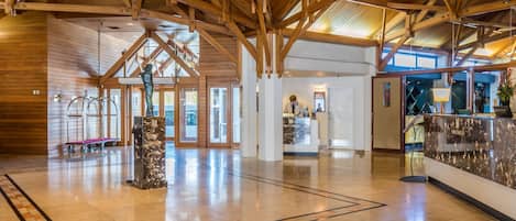 A spacious lobby with a high wooden ceiling, a reception desk, and a marble pillar.